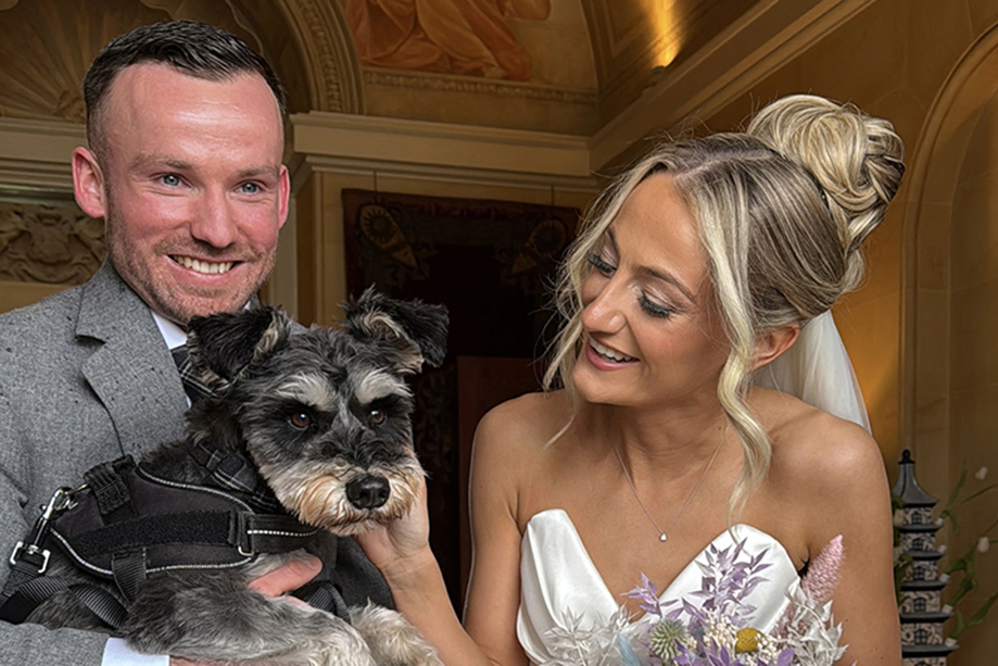Bride and groom smile while groom holds dog